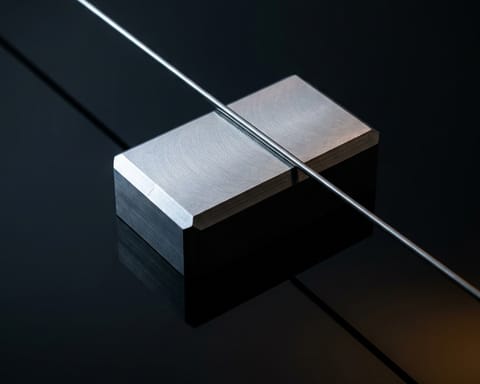 Abstract editorial image of a metal block and a tensioned string.